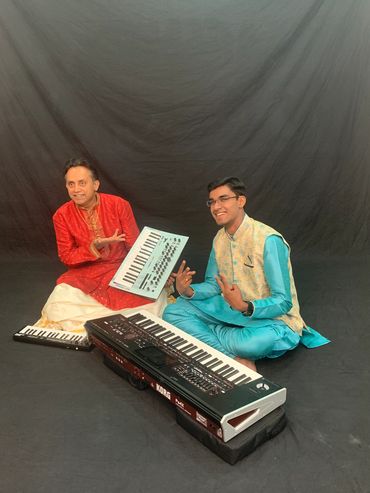 Two men in traditional attire with keyboards, posing on a black backdrop.