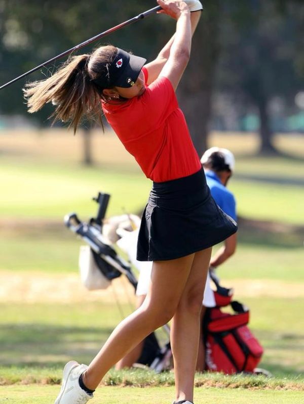 Female golfer in red shirt swinging a golf club on a sunny day.