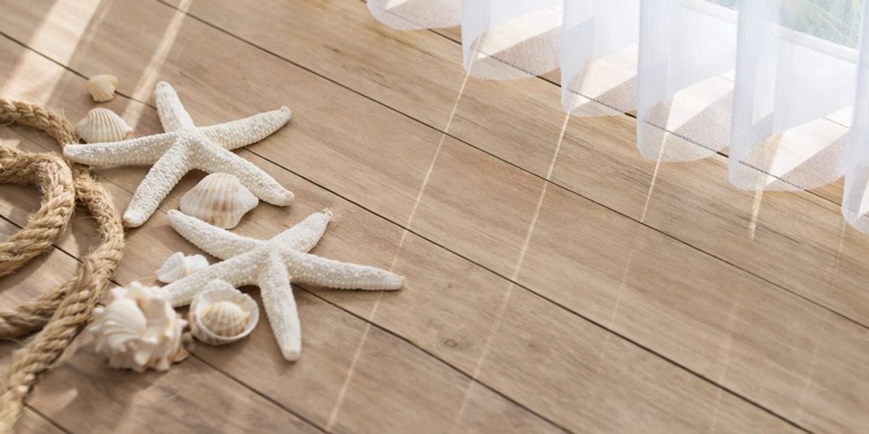 Starfish and seashells on a wooden floor near a sheer curtain.