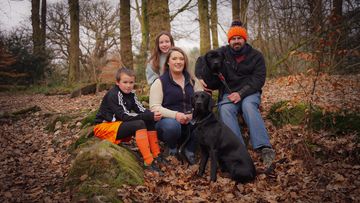 Family of four with two black dogs in a forest.
