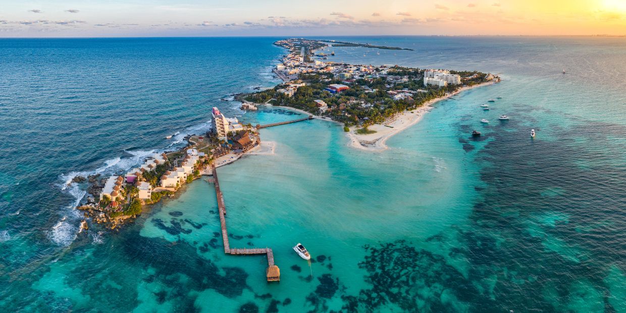 Aerial view of a tropical island with clear blue waters and boats at sunset.