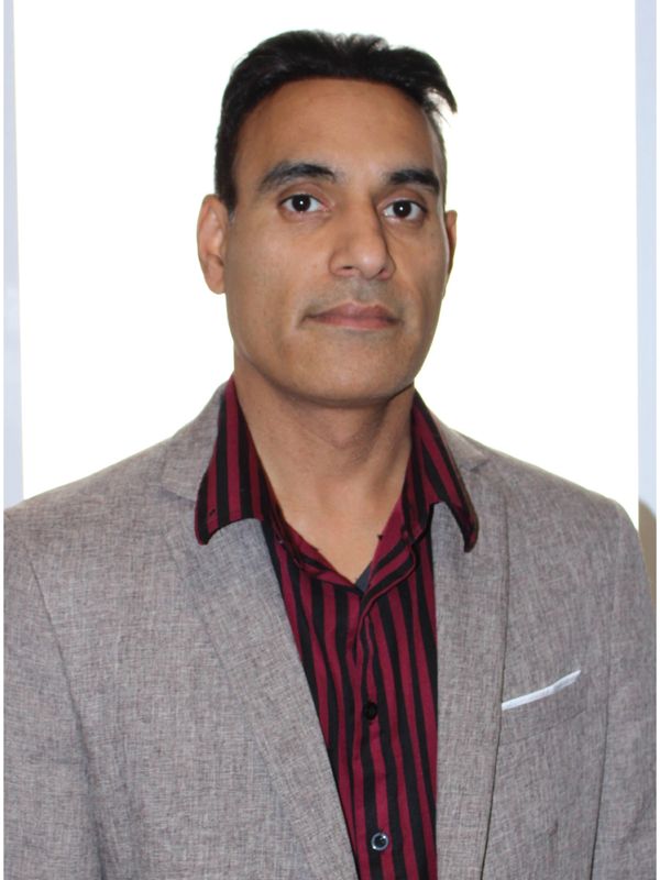 Man in a gray blazer and striped maroon shirt posing against a white background.