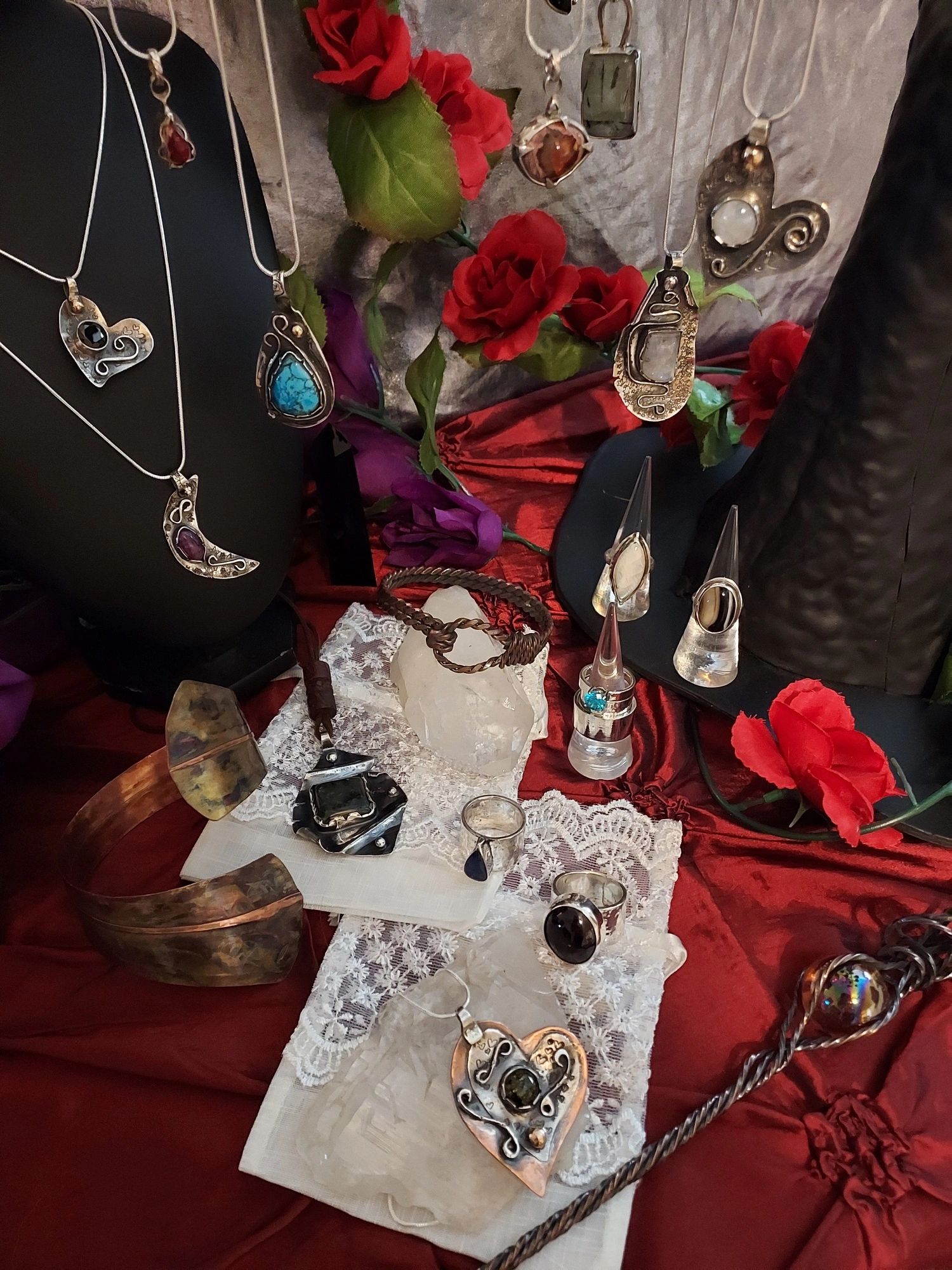 Handcrafted jewelry with gemstones displayed on red fabric and decorated with artificial roses.