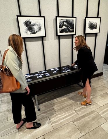 Two women interacting near a table with cards under abstract black and white paintings.