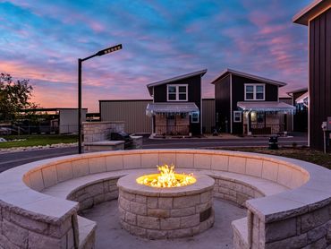 Stone fire pit with circular seating at sunset in front of modern houses.