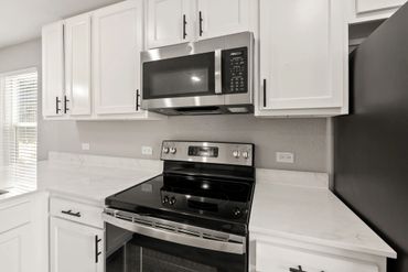 Modern kitchen with stainless steel stove and microwave, white cabinets, and marble countertops.