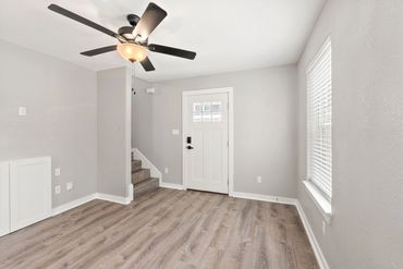 Bright empty room with wooden floors, a ceiling fan, and a white door.