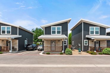 Modern black and stone duplex homes under blue sky with parked cars.