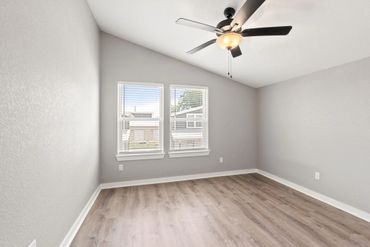 Empty room with wooden floor, gray walls, ceiling fan, and two windows.
