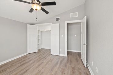 Empty room with gray walls, wood flooring, ceiling fan, and open closet doors.