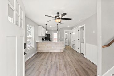 Modern kitchen and living area with wood flooring and ceiling fan.