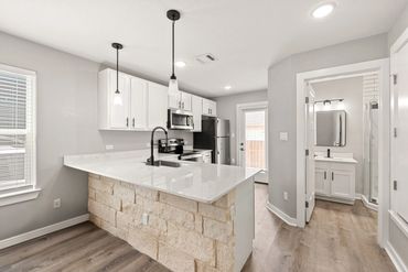 Modern kitchen with white cabinets, stone island base, and stainless steel appliances.