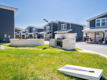 Modern townhouses with a grassy courtyard featuring a grill and cornhole boards.
