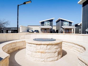 Outdoor stone fire pit seating area with modern houses in the background.