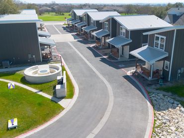 Modern townhouses with metal roofs lining a curved road and a small fire pit area.