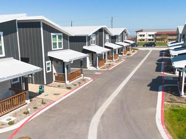 Modern townhouse complex with gray siding, white roofs, and small front porches along a paved street.