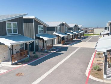 Modern row of townhouses with gray siding and metal roofs on a clear day.