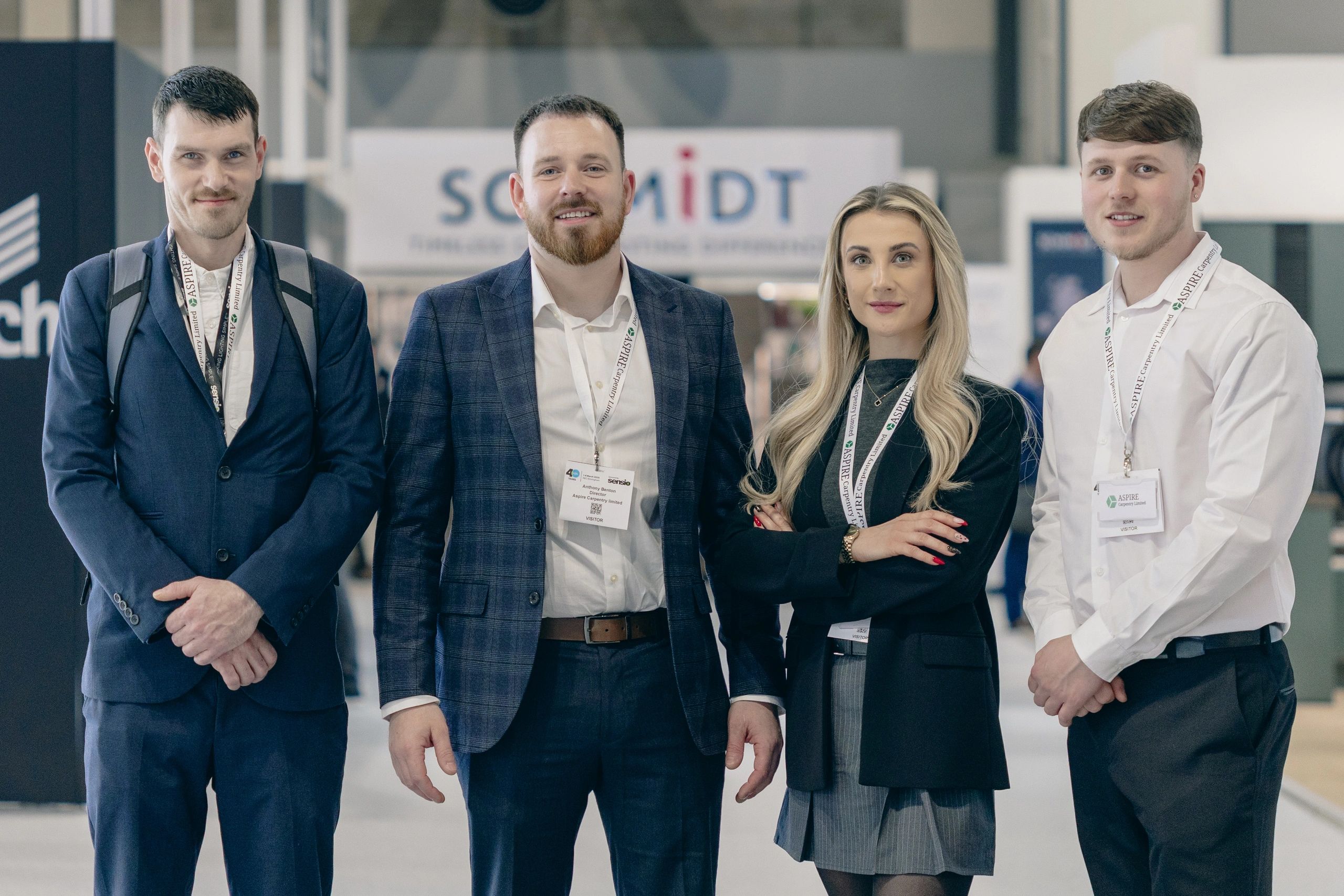 Four professionals posing at a business event with badges and lanyards.