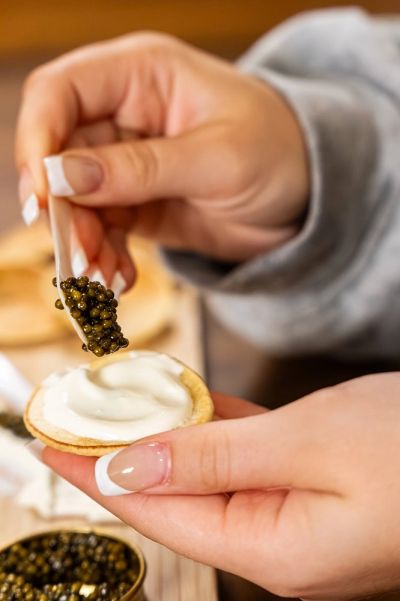 Ossetra caviar being served on a blini with crème fraîche using a mother-of-pearl spoon at King Cavi