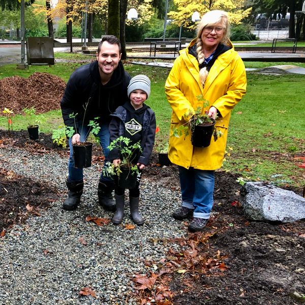 Three people holding small plants, ready for gardening outdoors.