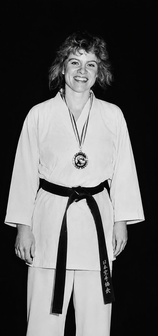 Woman in karate uniform with black belt and medal, smiling.