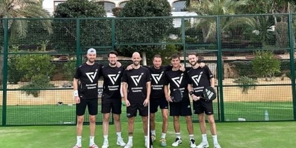 Six men in matching sportswear posing on a paddle tennis court.