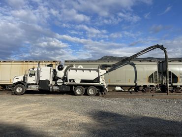 A vacuum truck positioned next to railcars under a partly cloudy sky.