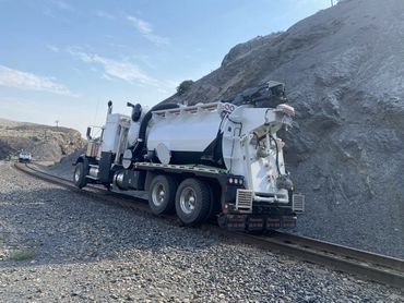 A specialized truck driving on railway tracks in a rocky area.