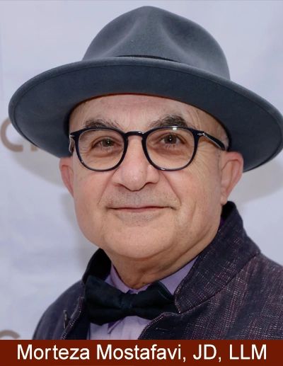 A man wearing glasses, a gray hat, and a bow tie, smiling gently.
