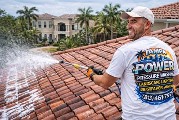 A man pressure washes a tiled roof wearing a Tampa Power shirt.