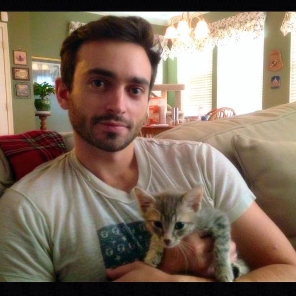 A man sitting on a couch holding a small tabby kitten.