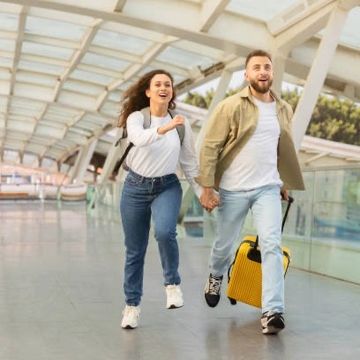 Happy couple running through an airport with luggage.