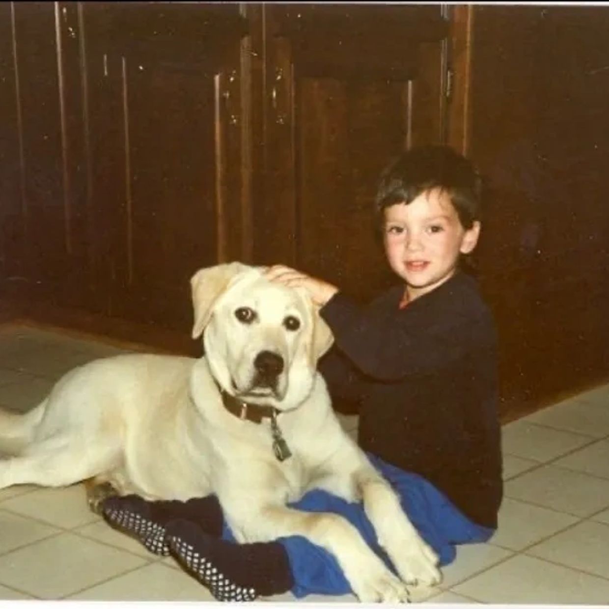 A young boy sitting on the floor petting a large white dog.