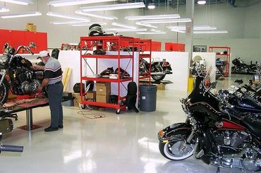 Man working on motorcycle in a clean, organized garage with several bikes and tools.