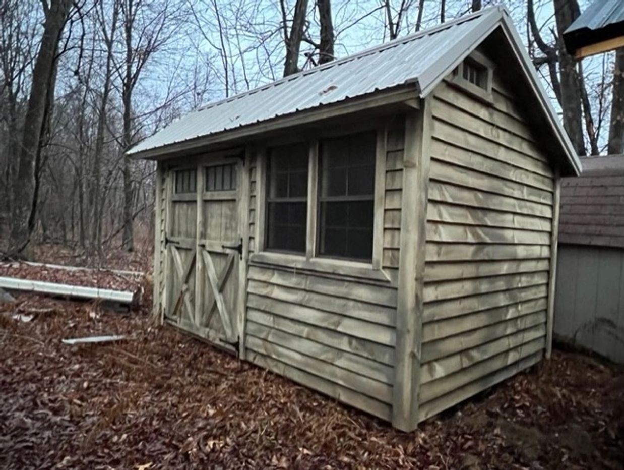 Weathered wooden shed in a leaf-covered forest clearing.