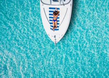Barco en el Caribe con una mujer tomando el sol en la cubierta, rodeado de un mar tranquilo y azul i
