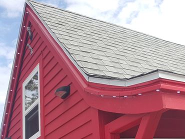 Close-up of a red house's roof and window under a partly cloudy sky.