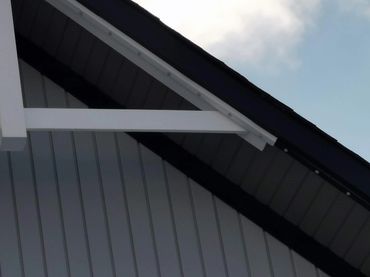 Gable roof with white truss and vertical siding under a cloudy sky.