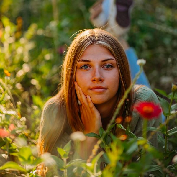 Young woman lying in a flower field, resting her face on her hand.