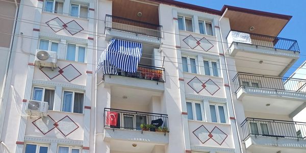 Apartment building with balconies, air conditioners, and a Turkish flag under a clear blue sky.