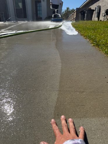 Person pressure washing a concrete driveway on a sunny day.