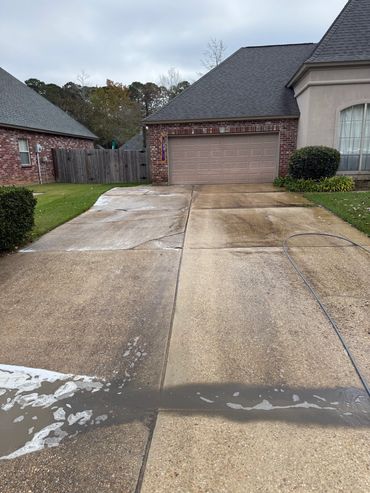 Driveway half cleaned with a pressure washer and a hose.