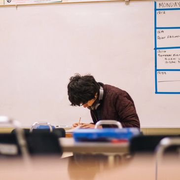Student focused on writing in a classroom with a whiteboard behind.