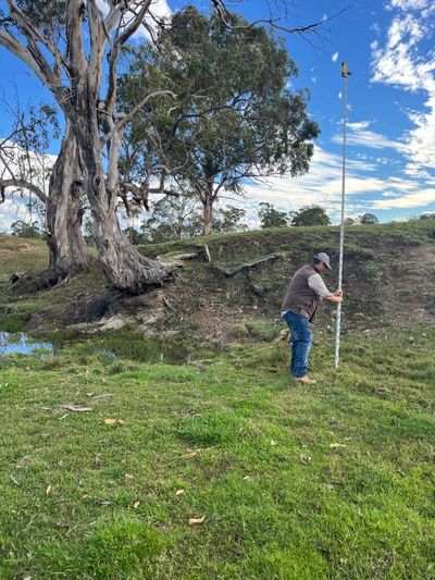 A person measuring land with a tall pole under clear skies.