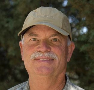 Smiling man with a mustache and beige cap.
