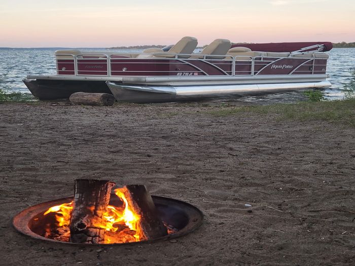Pontoon rental on Upper Whitefish Lake in Cross Lake having a campfire waiting for sunset.