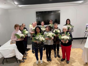 Group of women holding white Christmas arrangements at a flower workshop in Kamloops.