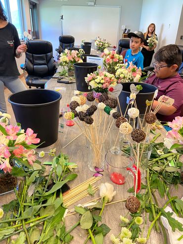 Youth flower workshop participants creating colorful floral centerpieces, learning flower arranging