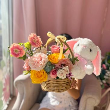 Cesta de flores coloridas con peluche de conejo.
