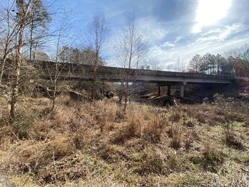 A bridge over a dry, grassy area with leafless trees and a partly cloudy sky.